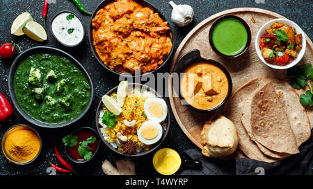 Indische Küche Gerichte: Tikka Masala, dal, Paneer, Samosa, chapati, Chutney, Gewürze. Indische Küche auf dunklem Hintergrund. Sortiment indisches Essen Top View oder flach. Stockfoto