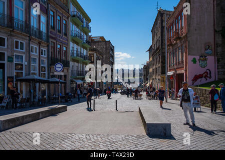 Menschen, die an einem sonnigen Tag an einer lebhaften Fußgängerzone in Porto, Portugal, spazieren gehen, umgeben von bunten Gebäuden, Cafés und Geschäften Stockfoto
