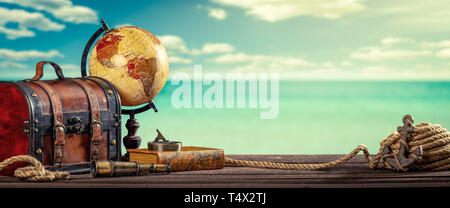 Vintage World Globe, Koffer, Kompass, Teleskop, Buch, Seil und Anker auf Dock mit Wasser, Wolken und Himmel Hintergrund - Travel Concept Stockfoto