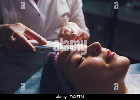 Hardware Kosmetologie. Kosmetikerin macht Farbtherapie Ultraschall Reinigung Gesicht des Kunden. Haut porentief reinigen. Anti-aging-Behandlungen. Spa. Nicht Stockfoto