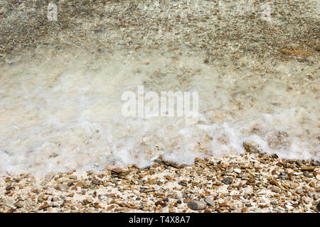 Weiche Wellen mit Schaum von Wasser auf Kies- und Sandstrand. Stockfoto
