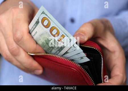 Bar bezahlen oder Shopping Konzept, Geldbörse mit US-Dollar in männlichen Händen. Mann im blauen Hemd, das Geld aus dem roten Leder Geldbörse Stockfoto