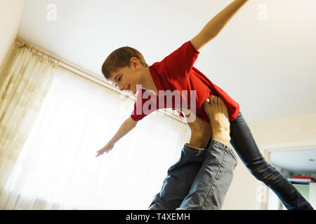 Der junge zeigt ein Flugzeug mit ausgestreckten Armen, an den Beinen seines Vaters unterstützt. Stockfoto