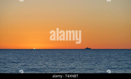 Orange Sonnenuntergang über dem Meer. Einsames Schiff am Horizont. Die Sonne verbirgt sich hinter dem Horizont im Meer. Stockfoto