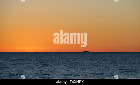 Orange Sonnenuntergang über dem Meer. Einsames Schiff am Horizont. Die Sonne verbirgt sich hinter dem Horizont im Meer. Stockfoto