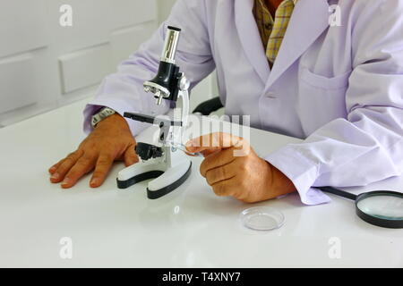 Die Forscher im weissen Anzug mit misroscope und Suchen mikroskopische Probe in seiner Hand. Stockfoto