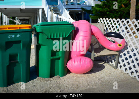 Eine große aufblasbare, pinke Flamingo-Schwimmfloatie sitzt seitwärts zwischen den Mülltonnen in einer Küstenresidenz in Florida in Boca Grande, FL, entfernt Stockfoto