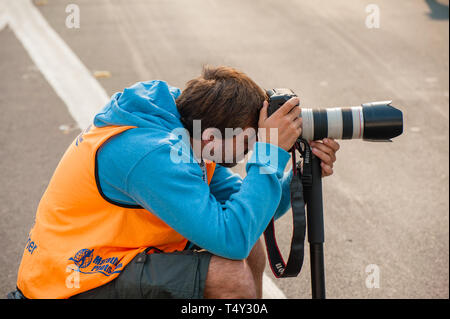 Sydney, Australien - 27. Oktober 2019: offizieller Fotograf crouching Fotografieren mit einer DSLR- und Zoom-objektiv, das Tragen von Hi-vis Gang bei einer Veranstaltung in Sydne Stockfoto