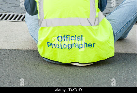 Die Rückseite eines offiziellen Fotografen sitzen, Fotografieren ein Ereignis, das Tragen eines Hi-vis yellow Weste Stockfoto