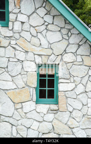 Kleine Holz- Fenster in einem Ferienhaus aus Stein mit grünen Giebel, Teil der Dachlinie angezeigt Stockfoto