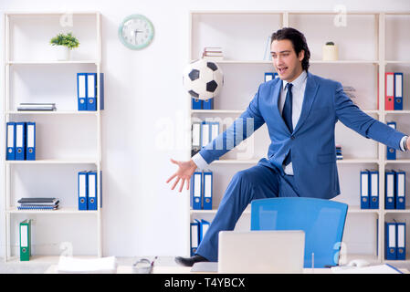 Junge gut aussehender Geschäftsmann mit Fußball im Büro Stockfoto