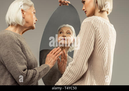 Angenehme schöne ältere Frau auf der Suche nach sich selbst Stockfoto