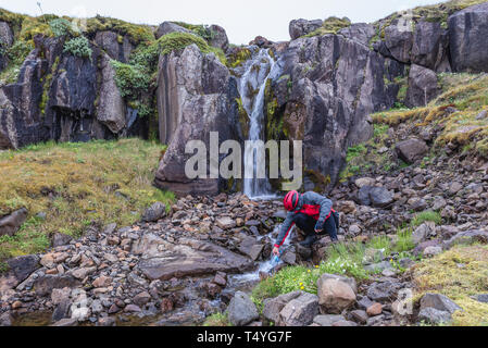 Der Mensch nimmt ein Wasser aus kleinen Wasserfall im Osten von Island Stockfoto