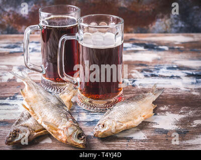 Dunkle Bier im Glas Tassen und getrocknete Fische auf einem Holztisch. Stockfoto