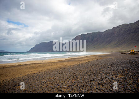 Der Strand von Famara auf Lanzarote in einem windigen Tag mit grauen Wolken und große Wellen Stockfoto