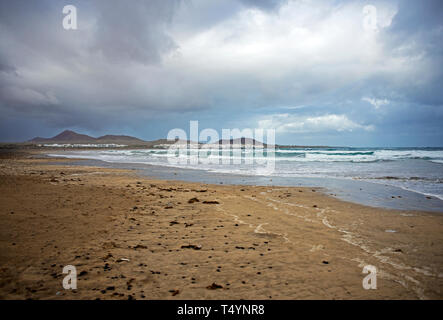 Der Strand von Famara auf Lanzarote in einem windigen Tag mit grauen Wolken und große Wellen Stockfoto