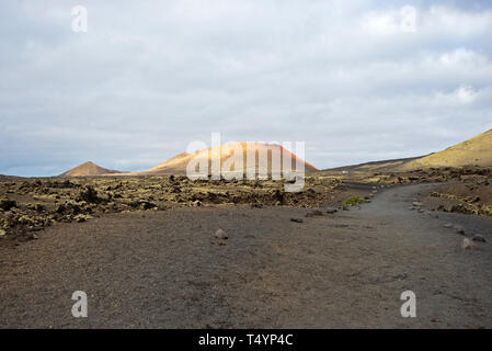 Vulkanische Landschaft auf der Insel Lanzarote, Kanarische Inseln, mit Montana Colorada, einem rot gefärbten erloschenen Vulkan, im Hintergrund Stockfoto