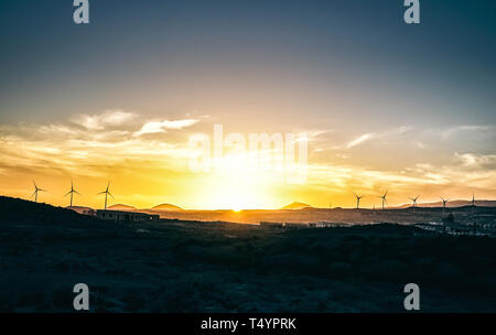 Panoramablick auf einen Sonnenuntergang über Hügel mit Bergen und Windenergieanlagen im Hintergrund - Vignette bearbeiten im Himmel - malerische Landschaft Grüne Energie Stockfoto