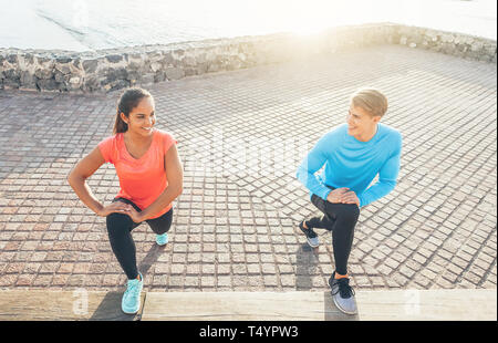 Joggen Paar stretching Beine beim Lächeln einander - Sportliche junge Menschen eine Ausbildung bei Sonnenuntergang Outdoor - Sport, Beziehung, Lifestyle Konzept Stockfoto