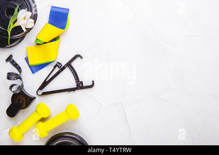 Ansicht von oben Bild von Kurzhanteln, bunte elastische Gummi Expander, Bremssättel und Maßband auf einem weißen strukturierten Hintergrund. Gesunder Lebensstil, Fitnessraum und nicht Stockfoto