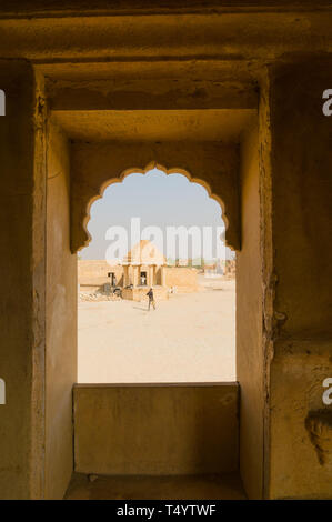 Das Schauen aus einem gewölbten Stein Fenster der Rajasthani Designs auf die unheimlichen Ruinen des Kumbalgarh Jaisalmer, Rajasthan, Indien. Dieses beliebte touristische Destina Stockfoto