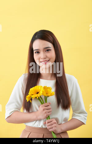 Glückliche junge Frau mit Blumenstrauß in der Hand auf gelbem Hintergrund Stockfoto