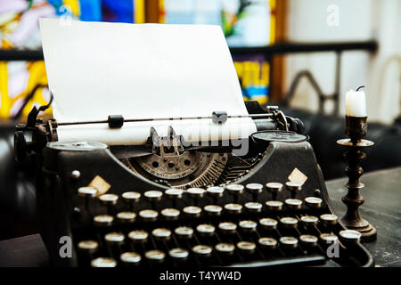 Close-up alte antike Schreibmaschine mit Papier auf dem Tisch des Schriftstellers vor dem hellen Buntglasfenster. Stockfoto