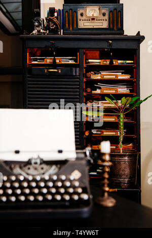 Alte antike Schreibmaschine auf dem Tisch des Schriftstellers vor der alten Küchenschrank mit Papieren. Stockfoto