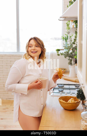 Köstliches Gebäck. Freudige nett lächelnden Frau, während sie ein Croissant aus dem Korb in der Küche Stockfoto