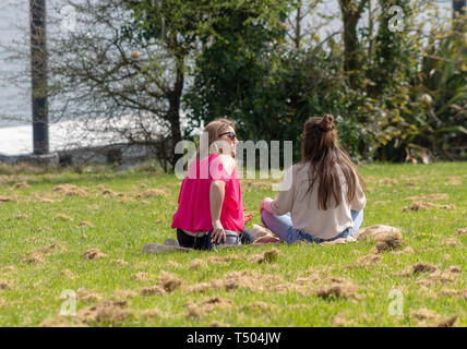 2 Junge Frauen Mädchen saßen auf dem Gras in einem Park in der Sonne. Stockfoto