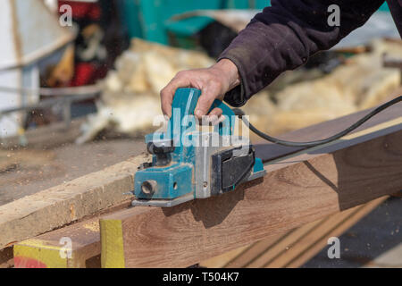 Tischler shipwright mit einem elektrischen Ebene auf eine Planke aus Teakholz Stockfoto