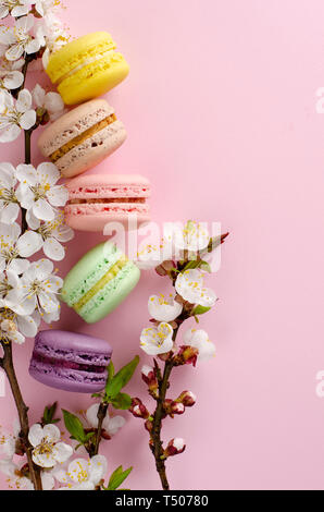 Bunte französische Macarons oder Makronen mit blühenden Blumen auf apricot Pastell rosa Hintergrund eingerichtet. Keine Diät Tag und Muttertag Konzept. Feder t Stockfoto