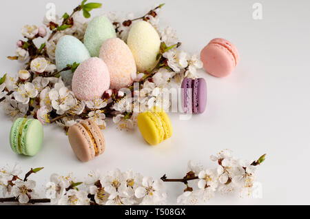 Dekorative Ostereier und süßen Macarons oder Makronen mit blühenden Aprikosen Blumen auf weißem Hintergrund eingerichtet. Kopieren Sie Platz. Grußkarte Konzept Stockfoto