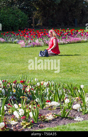 Bournemouth, Dorset, Großbritannien. April 2019. UK Wetter: Heiß und sonnig in Bournemouth - Frau, die den Sonnenschein unter den bunten Blumen in Bournemouth Lower Gardens genießt. Rosa weiß und blau vergessen mich nicht, Tulpen und Narzissen. Quelle: Carolyn Jenkins/Alamy Live News Stockfoto