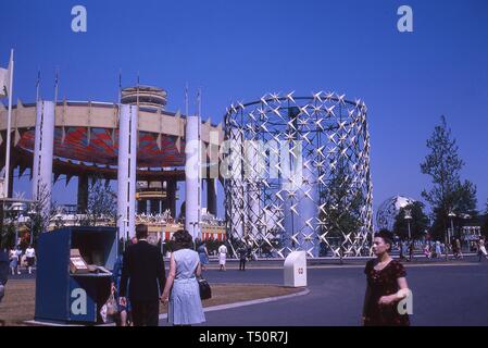 Mehrere Personen Ansatz einen Stand mit Flyer, an einem sonnigen Tag, in der Nähe von einem Brunnen, der Staat New York Pavillon und die Unisphere, in New York World's Fair, Flushing Meadows Park, Queens, New York, Juni 1964. () Stockfoto