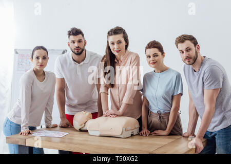 Gruppe von Personen bei Kamera schaut während der CPR Training mit Dummy Stockfoto