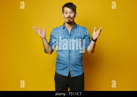 Junger Mann, stilvolle Hipster mit Bart und Schnurrbart in modischen Jeans shirt auf gelben Hintergrund überrascht, isoliert. Stockfoto
