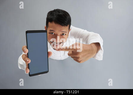 Happy asiatischer Mann Punkt auf grauem Hintergrund über der oberen Ansicht isoliert auf Smartphone Stockfoto