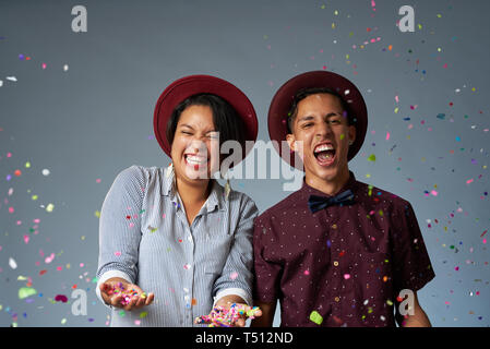 Glückliches junges Paar mit Konfetti fliegen Um auf Grau studio Hintergrund Stockfoto