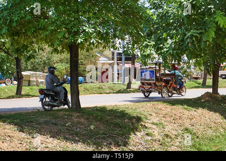 Kambodschanisches Tuk-tuk (remorque) Fahrer- und Motorradfahrer auf der Landstraße in Richtung Angkor Archäologischer Park in der Nähe von Siem Reap, Kambodscha. Stockfoto