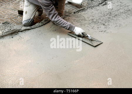 Bauarbeiter auf seinen Knien Abflachung Zementmörtel mit Spachtel, während eine konkrete Boden Stockfoto