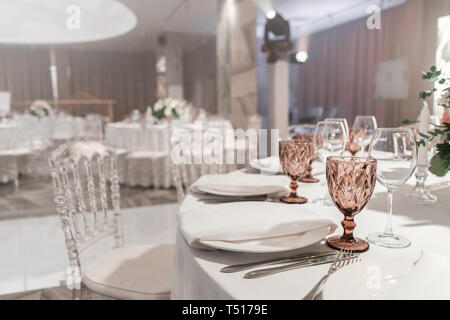 Weingläser auf runden Bankett Tisch serviert. Innenraum des Restaurant für Hochzeitsessen, bereit für die Gäste. Mit Blumenschmuck dekoriert. Gerichte Stockfoto
