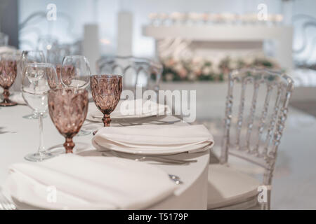 Weingläser auf runden Bankett Tisch serviert. Innenraum des Restaurant für Hochzeitsessen, bereit für die Gäste. Mit Blumenschmuck dekoriert. Gerichte Stockfoto