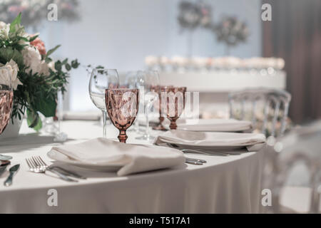 Gläser Wein auf runden Bankett Tisch serviert. Innenraum des Restaurant für Hochzeitsessen, bereit für die Gäste. Mit Blumenschmuck dekoriert. Gerichte Stockfoto