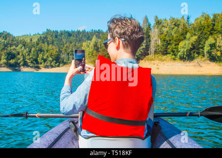 Selfie auf See. Junge Frau, Selbstportrait mit smart phone in Kajak auf lokvarsko See in Gorski kotar, Kroatien. Frau genießen Abenteuerliche Stockfoto