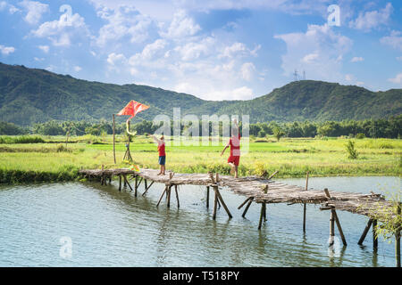 Phu Yen Provinz, Vietnam - Juli 9, 2017: In einer kleinen, ruhigen Dorf in Phu Yen Provinz, Vietnam, spielen Kinder Drachen, Radfahren auf einer Brücke gemacht Stockfoto