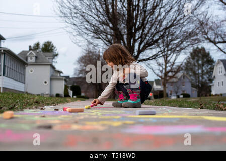 Ein kleines Mädchen, zieht auf einem Bürgersteig mit sidewalk Chalk bei warmem Wetter. Stockfoto