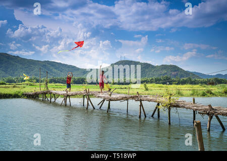 Phu Yen Provinz, Vietnam - Juli 9, 2017: In einer kleinen, ruhigen Dorf in Phu Yen Provinz, Vietnam, spielen Kinder Drachen, Radfahren auf einer Brücke gemacht Stockfoto