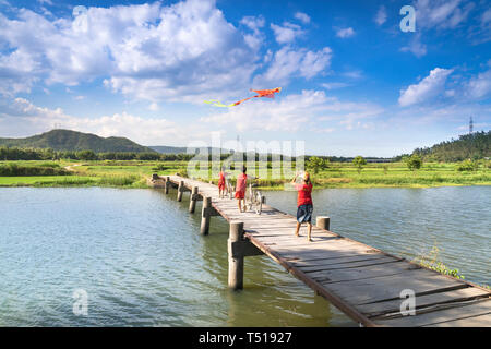 Phu Yen Provinz, Vietnam - Juli 9, 2017: In einer kleinen, ruhigen Dorf in Phu Yen Provinz, Vietnam, spielen Kinder Drachen, Radfahren auf einer Brücke gemacht Stockfoto