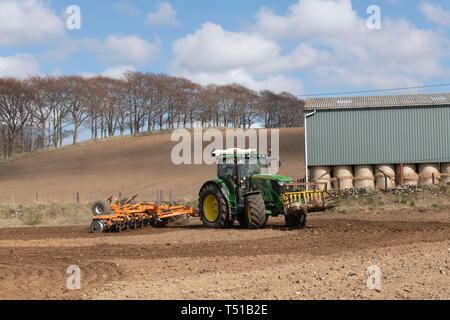 Eine grüne John Deere Traktor und ein Simba Unipress Kultivator bei der Arbeit in die schottische Landschaft, mit einer Linie der Buche am Horizont Stockfoto